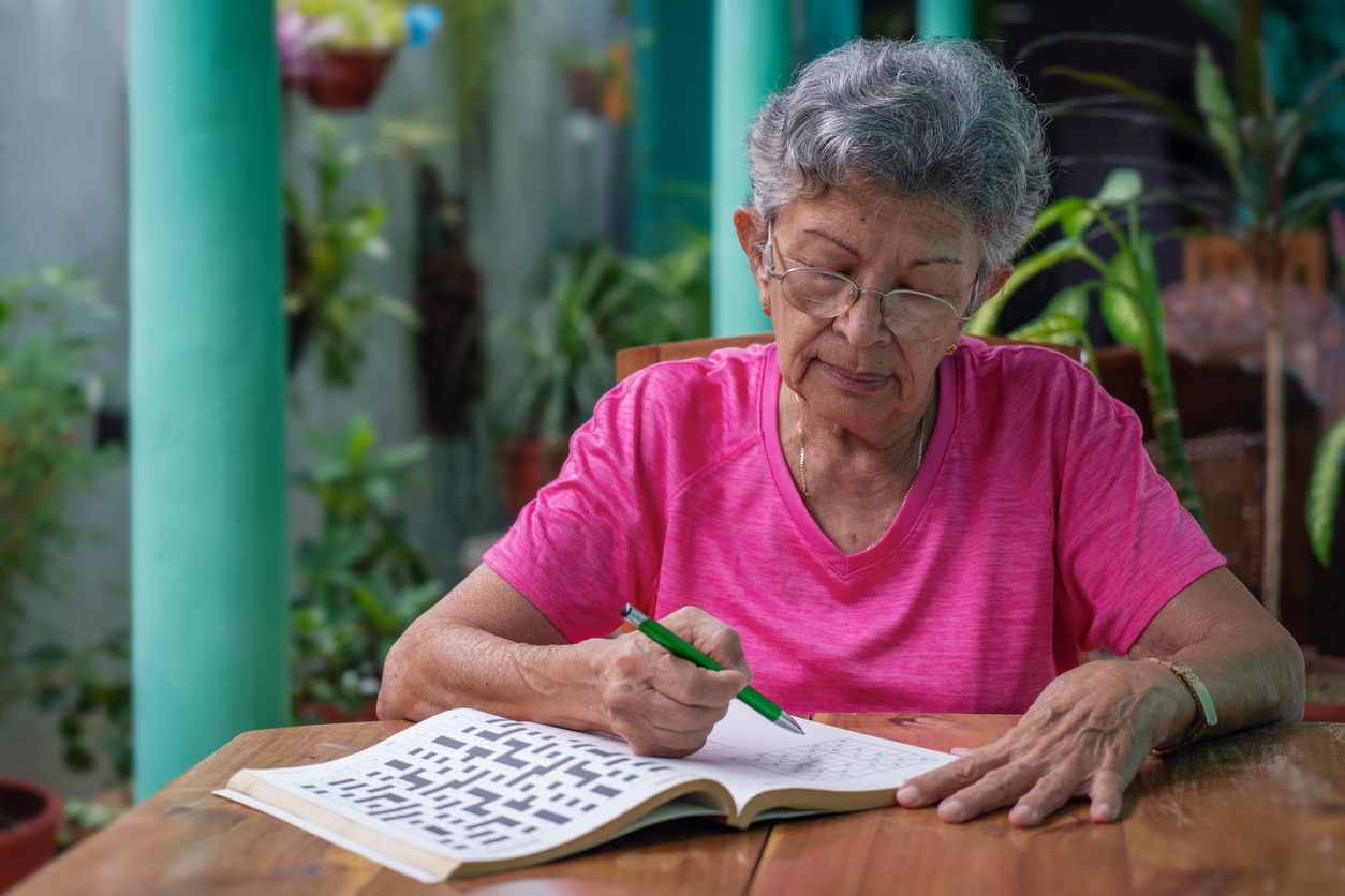 Senior woman with glasses sitting at a table, filling in sudoku