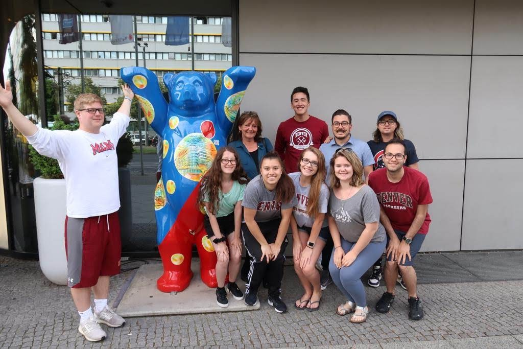 DU students posing together in front of a statue of a colorful bear