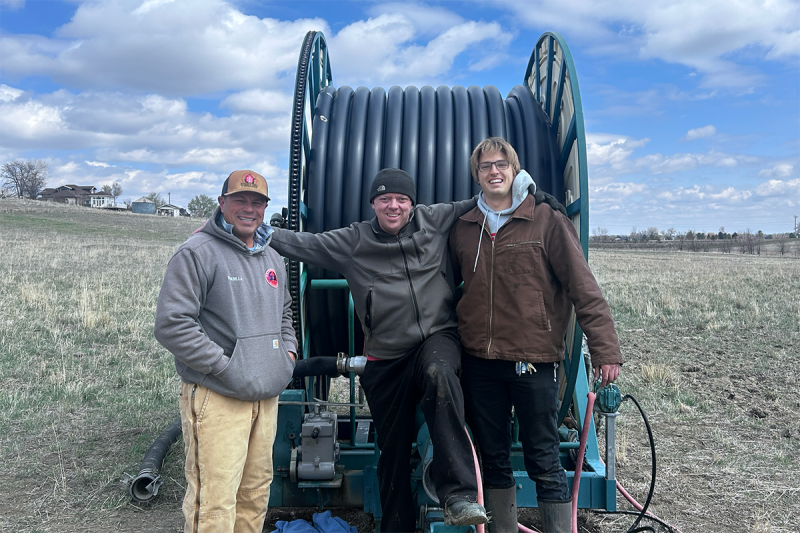 A farm employee, Justin Huff, and Uton Dellosso stand in front of the repaired farm equipment