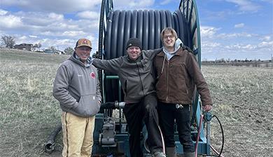 A farm employee, Justin Huff, and Uton Dellosso stand in front of the repaired farm equipment