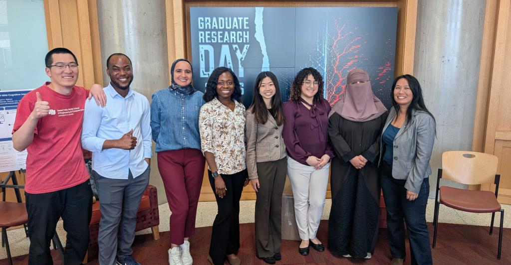 DU HCI students standing behind slide which says "grad research day"