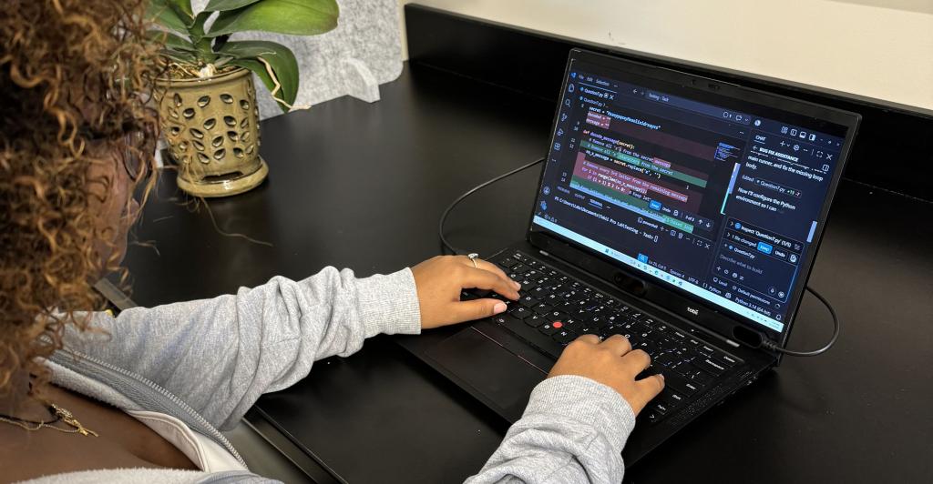 person sitting and working on laptop with code on the screen. Attached to the laptop is an eyetracking camera